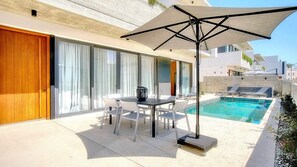 A poolside area with a table and chairs, a large umbrella, and a pool.