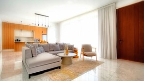 A modern living room with a sectional sofa, a coffee table, and a dining area with a kitchen in the background. - Villa Allegra Elite - Luxury Villa In Kato Paphos (Paphos)