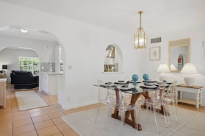 Ein modernes Interieur mit Essbereich, der einen Glastisch und Stühle umfasst, einer Küche im Hintergrund und einem Wohnzimmer mit einer Couch.