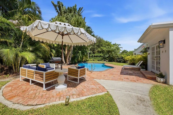 Ein Garten mit Swimmingpool, Grill und Gartenmöbel mit Tisch und Stühlen.