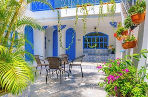 Un patio con una mesa y sillas, puertas azules y plantas en macetas.