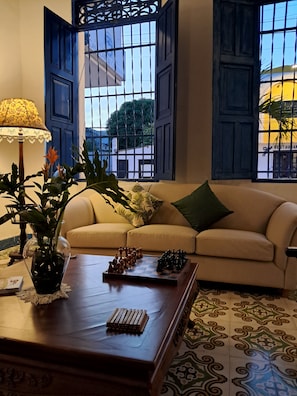 Una sala de estar con un sofá, una mesa de centro con piezas de ajedrez, una lámpara y un florero con plantas.