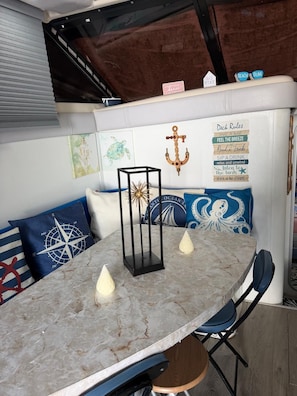 A nautical-themed seating area with a table, cushions, and wall decorations including a compass, anchor, and a sign with 'Deck Rules'.