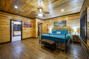 A wooden-paneled room with a bed, a bench, a ceiling fan, and a window with blinds. - A Beautiful View · New Listing! Ridgetop 5BR w/ Hot Tub, Game Room & Fire Pit (Broken Bow)
