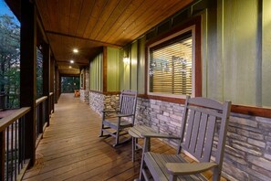 A covered porch with wooden flooring, stone walls, and two wooden benches. - A Beautiful View · New Listing! Ridgetop 5BR w/ Hot Tub, Game Room & Fire Pit (Broken Bow)