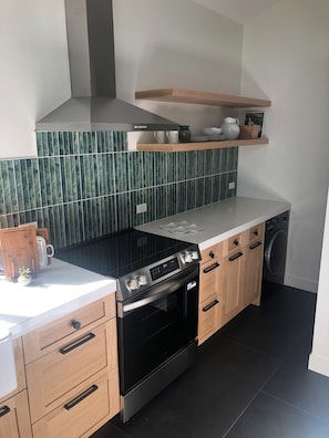 Ett modernt kök med en spis i rostfritt stål, träskåp, en inbyggd ugn och en tvättmaskin.