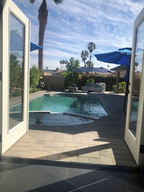 A pool area with a clear view of the sky, palm trees, and a stone wall. - Luxury 1-bedroom studio, pool, hot tub, 7 minutes from Coachella and stage coach (La Quinta)