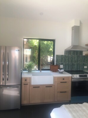 A modern kitchen with a built-in sink, stainless steel appliances, and a view of greenery outside. - Luxury 1-bedroom studio, pool, hot tub, 7 minutes from Coachella and stage coach (La Quinta)