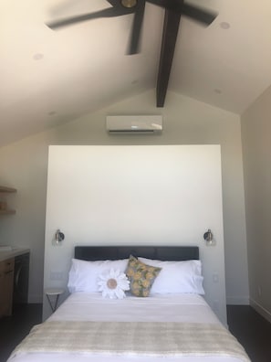 A bedroom with a bed, a ceiling fan, an air conditioning unit, and a nightstand with a lamp. - Luxury 1-bedroom studio, pool, hot tub, 7 minutes from Coachella and stage coach (La Quinta)