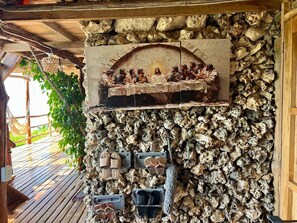 Un mur de pierre orné d’une fresque représentant la Cène, une terrasse en bois et un hamac suspendu.