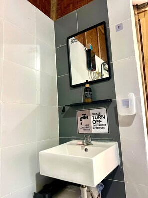 A bathroom with a white sink, a mirror, and a hand soap dispenser. There is a sign instructing to turn off the faucet to conserve water.