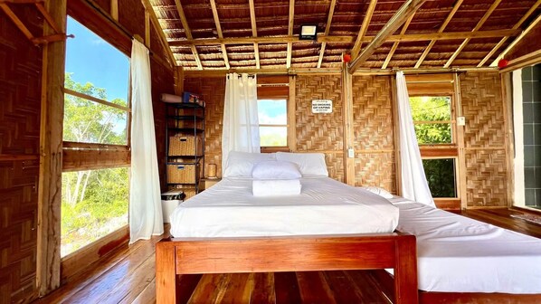 A wooden room with a bed, a shelf with baskets, and a window with a view of greenery.
