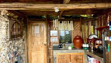 A rustic wooden interior with a stone wall, a wooden door, a kitchen area with a refrigerator, and a dining table with chairs.