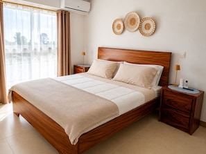 A modern hotel room with a wooden bed, beige bedding, a view through the window, and a wall-mounted air conditioner. - Azure Horizon Jaco - Beach & Ocean View Apartment (Jaco)