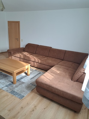 Ein Wohnzimmer mit einem braunen Ecksofa, einem Holztisch und einem grauen Teppich.