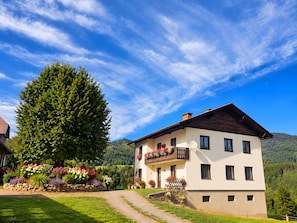 Ein zweistöckiges Haus mit Balkon, umgeben von einem Garten mit verschiedenen Pflanzen und Blumen.
