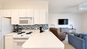 A modern kitchen with white cabinets, a microwave, and a stove. There is a flat-screen TV mounted on the wall and a brown leather chair. - Myrtle Beach Hideaway | 1BR | King Bed (Myrtle Beach)