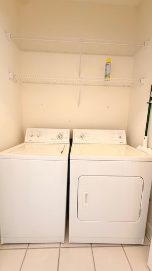 A laundry room with two front-loading washing machines and a shelf above. - Myrtle Beach Hideaway | 1BR | King Bed (Myrtle Beach)