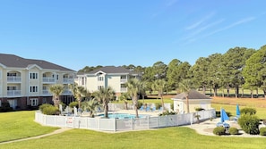 A residential complex with multiple two-story buildings, a swimming pool, and a fenced patio area with lounge chairs. - Myrtle Beach Hideaway | 1BR | King Bed (Myrtle Beach)