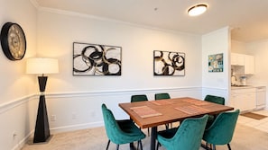 A dining area with a wooden table, green chairs, and abstract artwork on the wall. - Myrtle Beach Hideaway | 1BR | King Bed (Myrtle Beach)