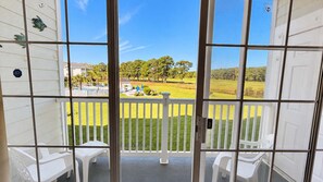 A balcony with a view of a grassy area and trees, white railings, and a pool with lounge chairs. - Myrtle Beach Hideaway | 1BR | King Bed (Myrtle Beach)