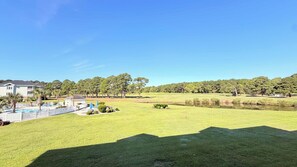 A residential area with a swimming pool, a fenced patio, and a large grassy field with trees in the background. - Myrtle Beach Hideaway | 1BR | King Bed (Myrtle Beach)