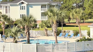 A pool area with lounge chairs and palm trees, surrounded by a white fence. - Myrtle Beach Hideaway | 1BR | King Bed (Myrtle Beach)