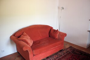 Un canapé rouge avec un coussin assorti, placé contre un mur uni, un tapis à motifs sur le sol et un interrupteur sur le mur.