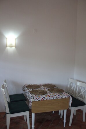 Un pequeño comedor con una mesa y dos sillas, una lámpara de pared y piso de baldosas.