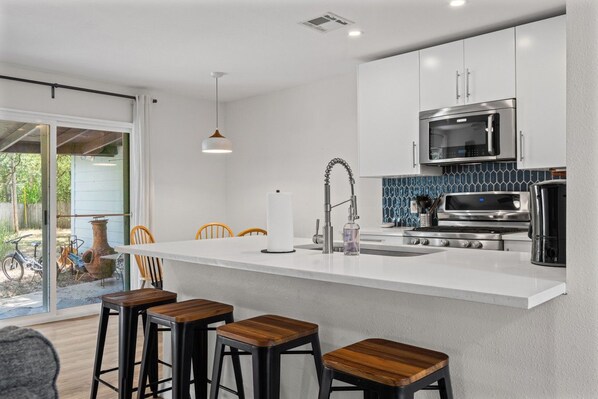 Una cocina moderna con una isla central, taburetes de bar, microondas y cafetera.