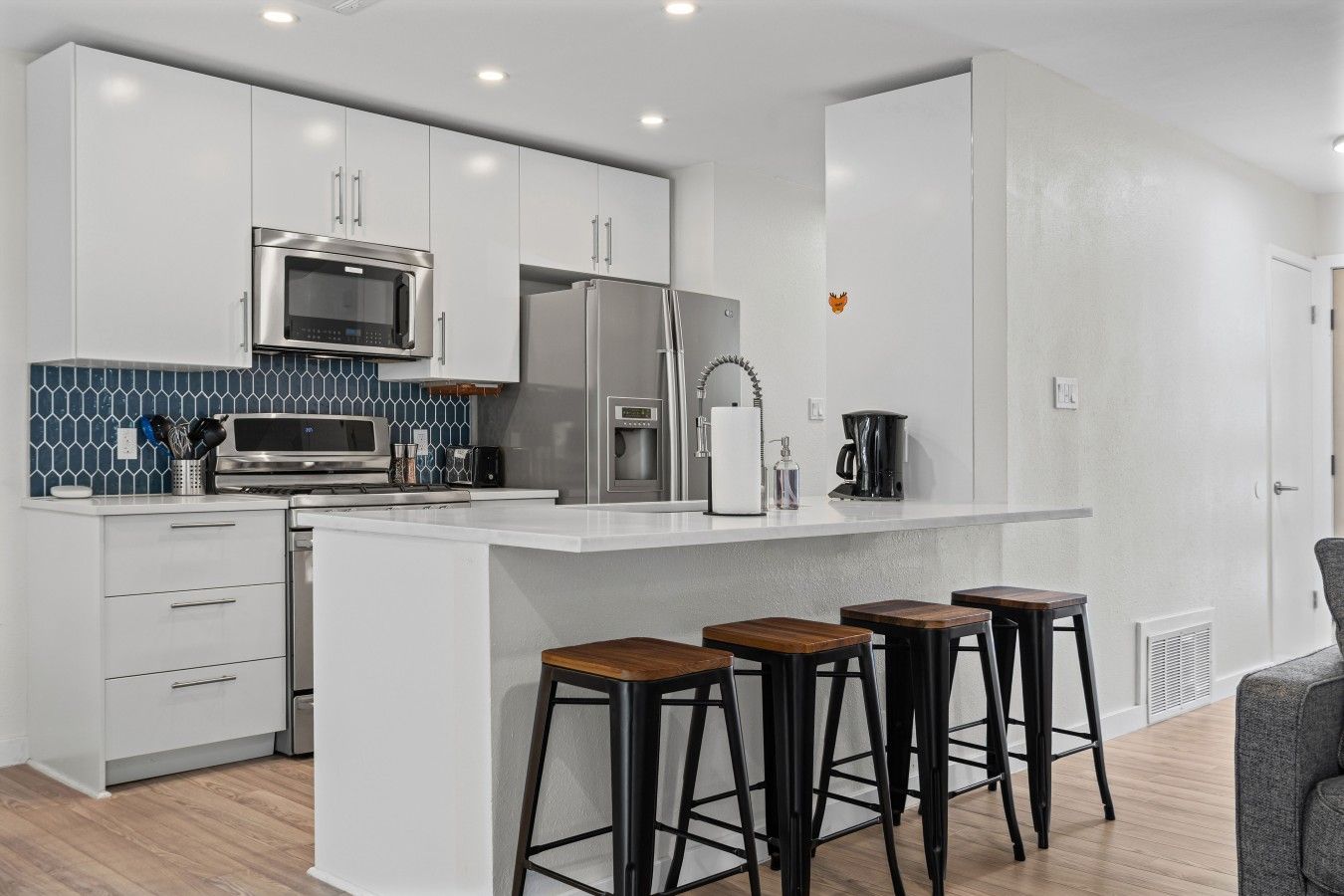 A modern kitchen with white cabinetry, a central island with stools, a microwave, a refrigerator, and a coffee maker.