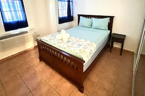 Een slaapkamer met een houten bed, een klein nachtkastje en een raam met gordijnen.