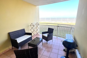 Een balkon met een bank, stoelen, een tafel en een barbecue.