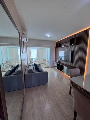 Ein modernes Wohnzimmer mit einer Couch, einem Essbereich mit Tisch und einem an einer Wand mit Holzpaneelen befestigten Fernseher.