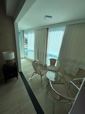 Une chambre d’hôtel avec un balcon, des fauteuils en osier, une petite table et une lampe.