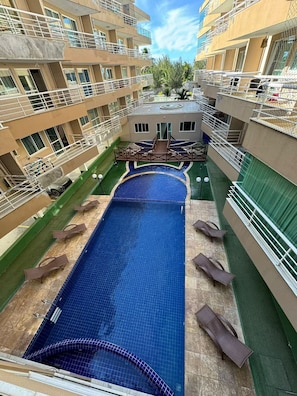 Ein mehrstöckiges Hotel mit einem zentralen Schwimmbad, Balkonen und einem kleinen Gebäude in der Mitte.