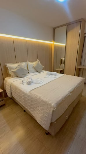 Ein ordentlich gemachtes Bett mit Kissen und einem zusammengerollten Handtuch, ein Nachttisch und ein großer Spiegel.