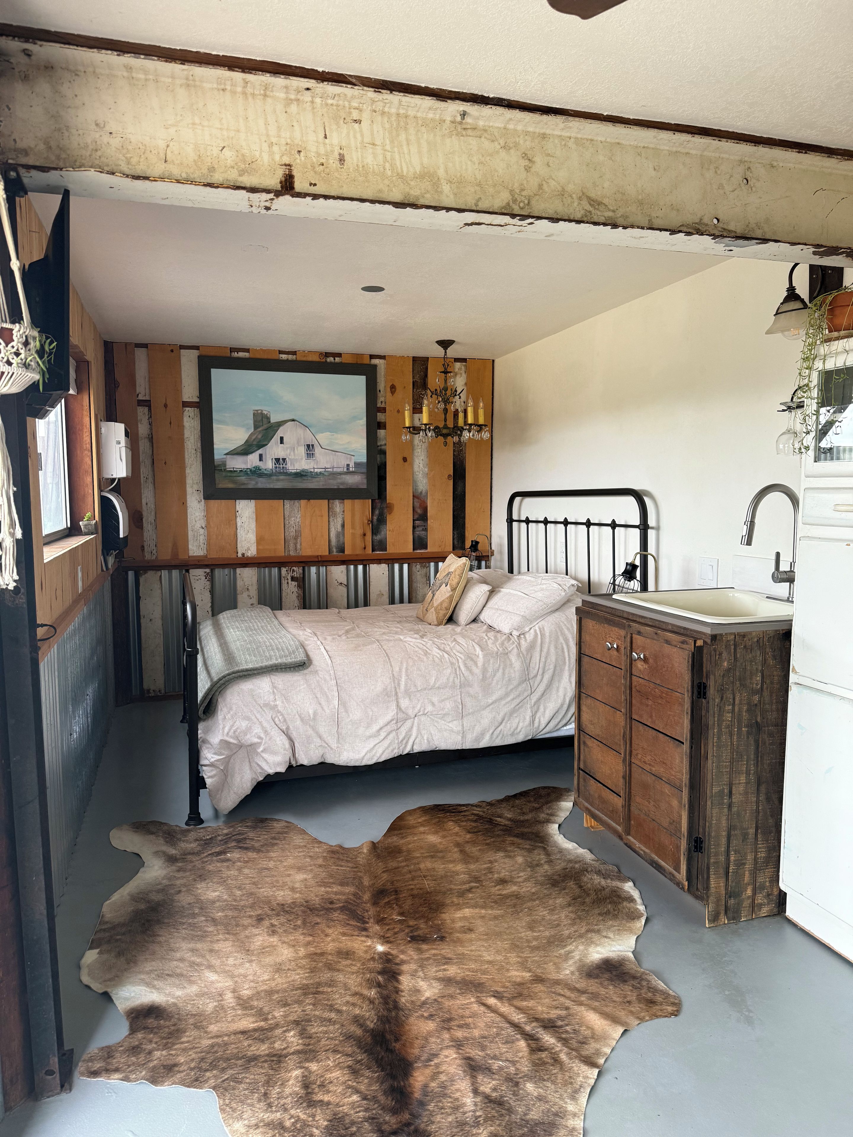 A rustic bedroom with a bed, a wooden cabinet, a sink, and a painting on the wall.