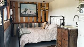 A rustic bedroom with a bed, a wooden cabinet, a sink, and a painting on the wall.