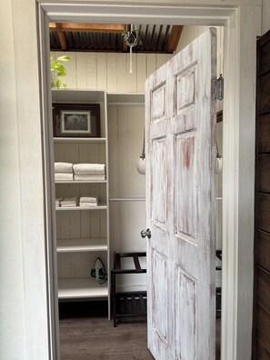 A hallway leading to a room with a rustic wooden door, a white shelving unit with folded towels, and a hanging plant. - The Atrium- Templeton Ranch Retreat - Private Patio - Farm Animals- Wine Country (Templeton)