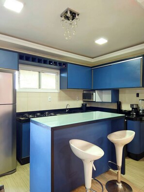 Une cuisine moderne avec des meubles bleus, un îlot central doté de tabourets, un four à micro-ondes et une cuisinière à gaz.