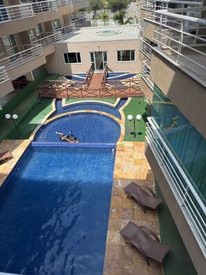 A rooftop swimming pool with a diving board, surrounded by a building with multiple balconies. - Cumbuco Beach Place 03 – Piscina + 100 metros Mar (Caucaia)
