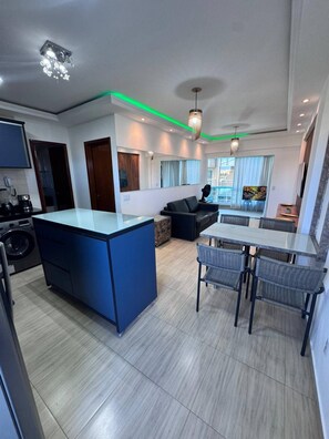 Une cuisine moderne dotée d’un îlot central, un coin repas avec une table et des chaises, et un espace de vie avec un canapé.