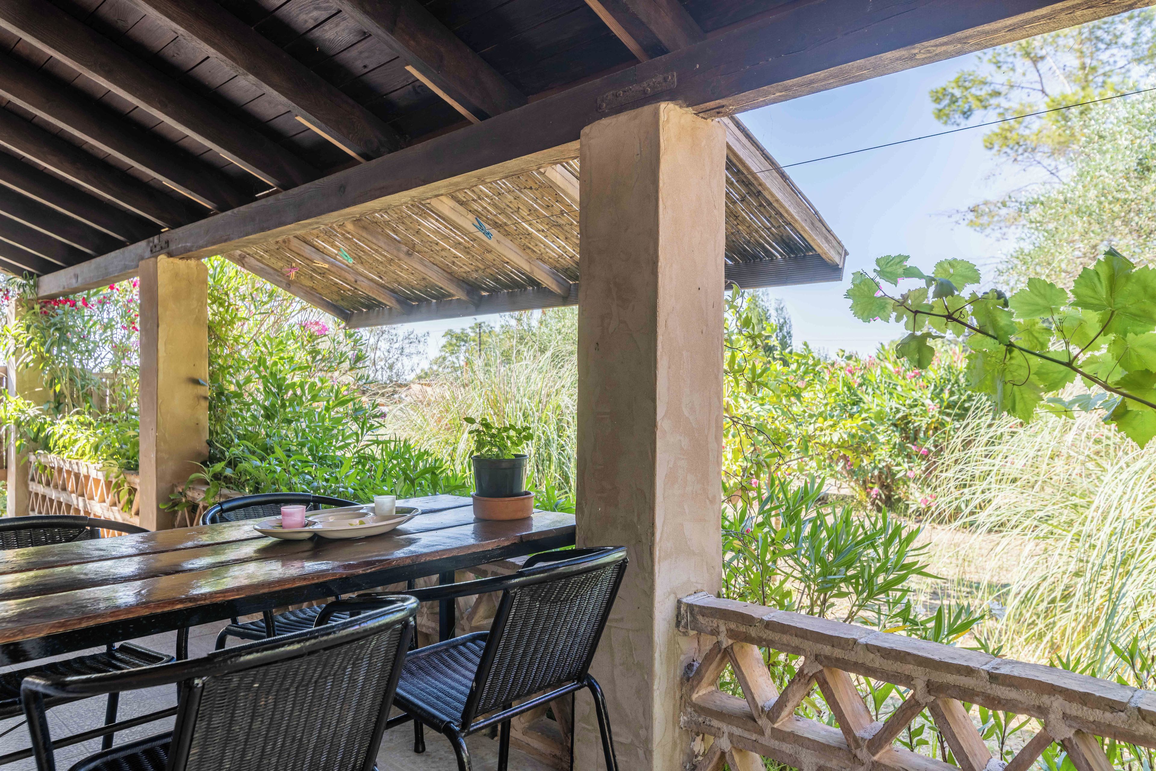 Eine Terrasse im Freien mit einem Holztisch und -stühlen, umgeben von üppigem Grün und einem Holzbalken.