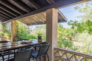 An outdoor patio with a wooden table and chairs, surrounded by lush greenery and a wooden railing.