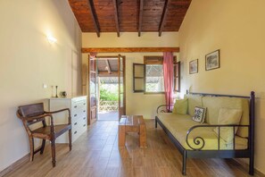 A room with a wooden ceiling, a bed with a metal frame, a wooden chair, a small table, and a white dresser.