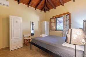A bedroom with a bed, a wardrobe, a chair, a desk, and a window with curtains. - Zanteva-Psophis Cottage, Zanteva Cottages (Zakynthos)