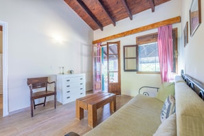 A room with a wooden bench, a white dresser, a bed with a green pillow, and a window with pink curtains.