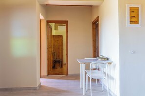 A hallway with a wooden door leading to another room, a white table with a chair, and a wall-mounted light switch.