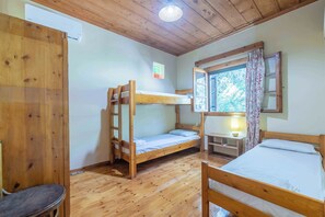 A room with wooden bunk beds, a small table with a lamp, and a window with curtains.